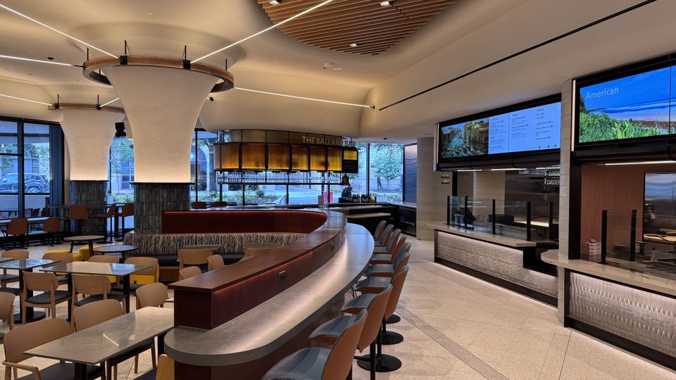 Interior of the National Geographic Museum of Exploration's Explorers Eatery with curved bar seating, tables, and digital menu displays, illuminated by ambient lighting.