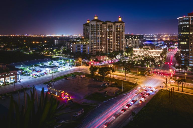 Nighttime cityscape with a tall, illuminated building, busy roads with light trails, and glow from streetlights and distant city lights.