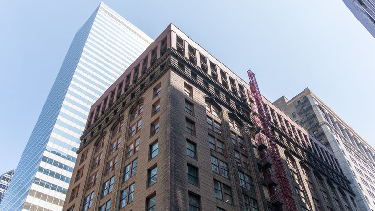 View of two contrasting buildings, one modern with glass panels, the other historic with brick facade and red fire escape, under a clear blue sky.