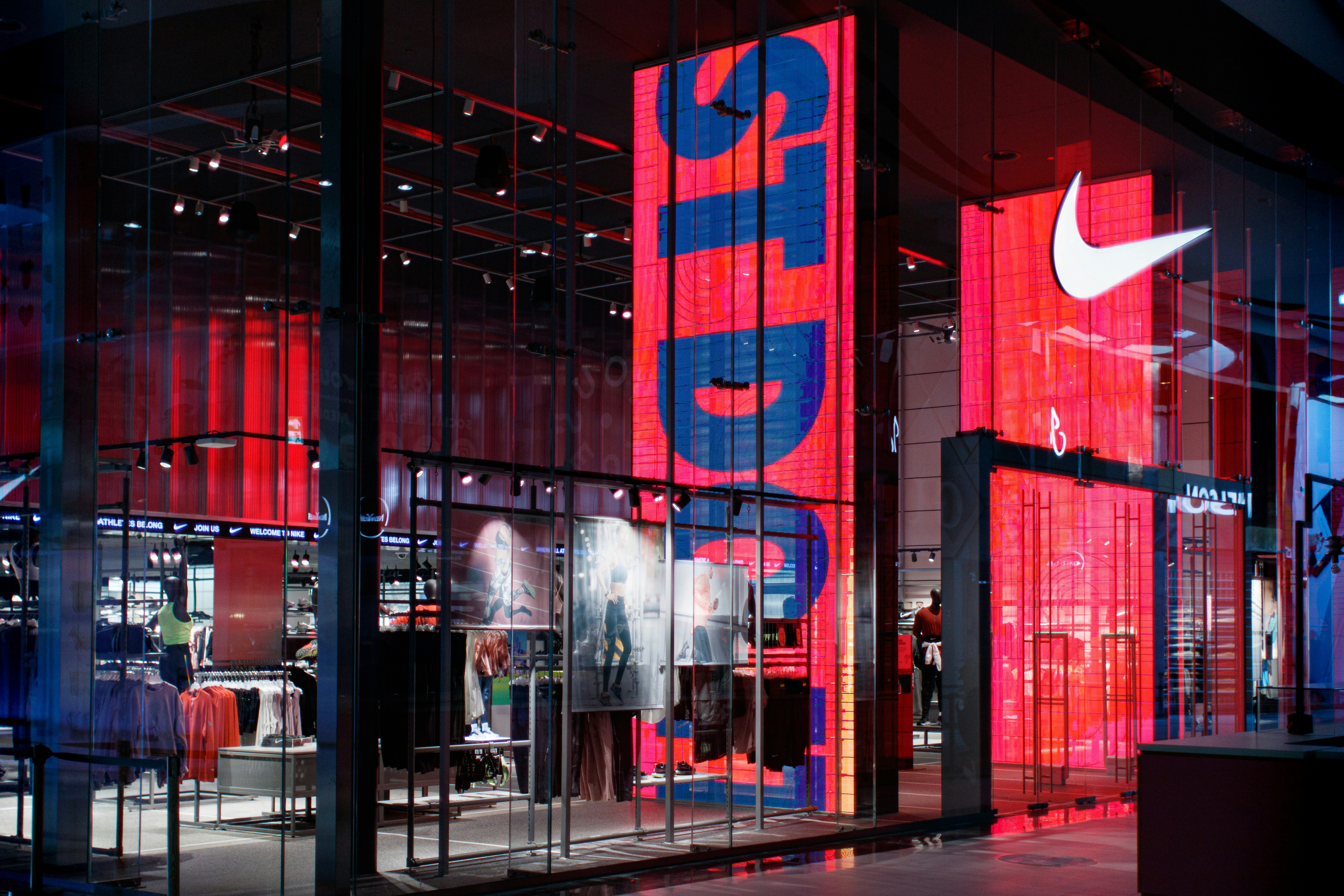 Storefront with large red and blue digital displays, showcasing athletic apparel and accessories inside.