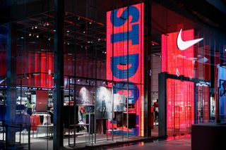 Storefront with large red and blue digital displays, showcasing athletic apparel and accessories inside.