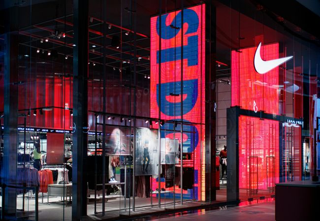 Storefront with large red and blue digital displays, showcasing athletic apparel and accessories inside.