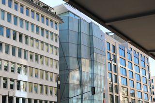 Modern buildings with glass facades, including a distinctive geometric structure, set against a clear sky.