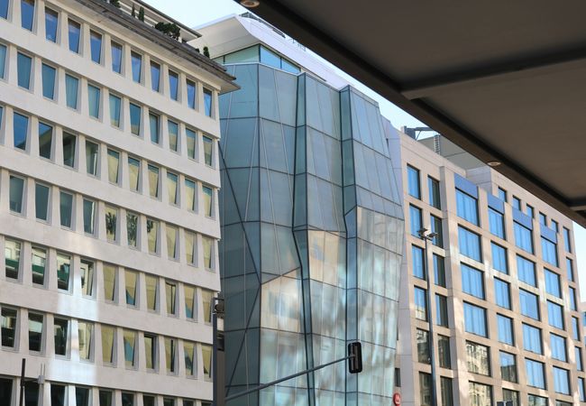 Modern buildings with glass facades, including a distinctive geometric structure, set against a clear sky.
