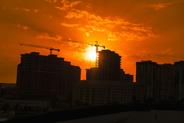 Construction cranes on top of buildings at sunset.