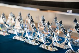 A row of clear crystal awards with "BISNOW" inscription on a blue tablecloth.