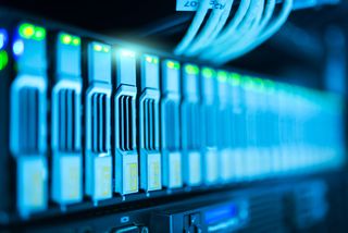 Close-up of illuminated server hardware with cables, showing rows of blue and green LED-lit hard drives in a data center.