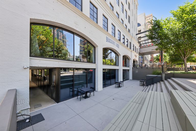 Exterior of a modern building with arched windows labeled "Brasserie Lundi," and an outdoor seating area with tables and chairs.