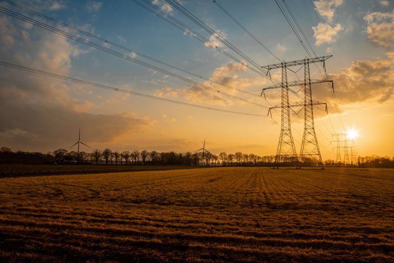 Power lines and wind turbines in a field at sunset, with a sunlit sky and scattered clouds.