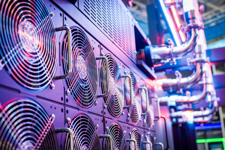 Close-up view of multiple cooling fans and metallic pipes with neon lighting in a data center or industrial setting.