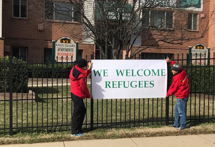 Employees hanging a 'We Welcome Refugees' sign at the Kings Square Apartments community in Maryland, managed by David Mendick. 