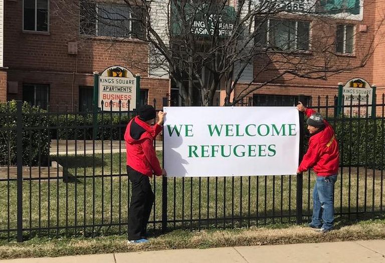 Employees hanging a 'We Welcome Refugees' sign at the Kings Square Apartments community in Maryland, managed by David Mendick. 