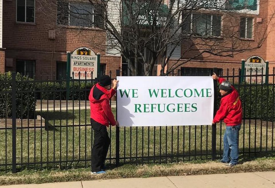 Employees hanging a 'We Welcome Refugees' sign at the Kings Square Apartments community in Maryland, managed by David Mendick.