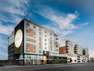 A modern midrise apartment complex with "Now Leasing" sign with ground level retail space.