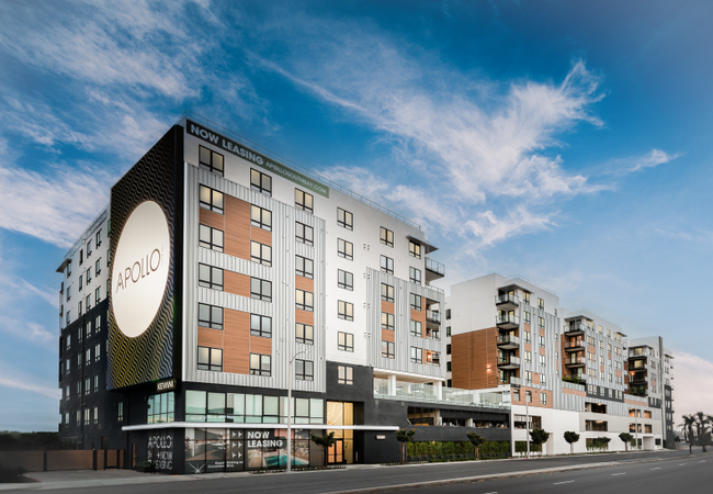A modern midrise apartment complex with "Now Leasing" sign with ground level retail space.