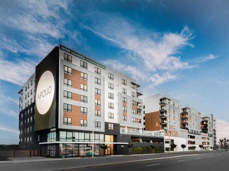 A modern midrise apartment complex with "Now Leasing" sign with ground level retail space.