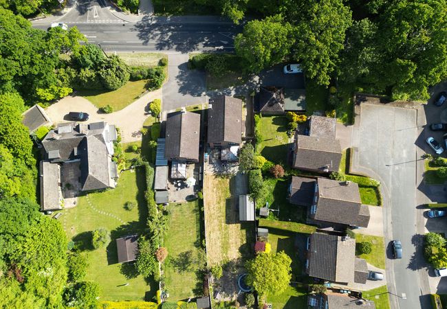 Aerial view of a suburban neighborhood with houses, backyards, trees, and parked cars on a clear day.