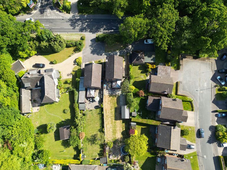 Aerial view of a suburban neighborhood with houses, backyards, trees, and parked cars on a clear day.