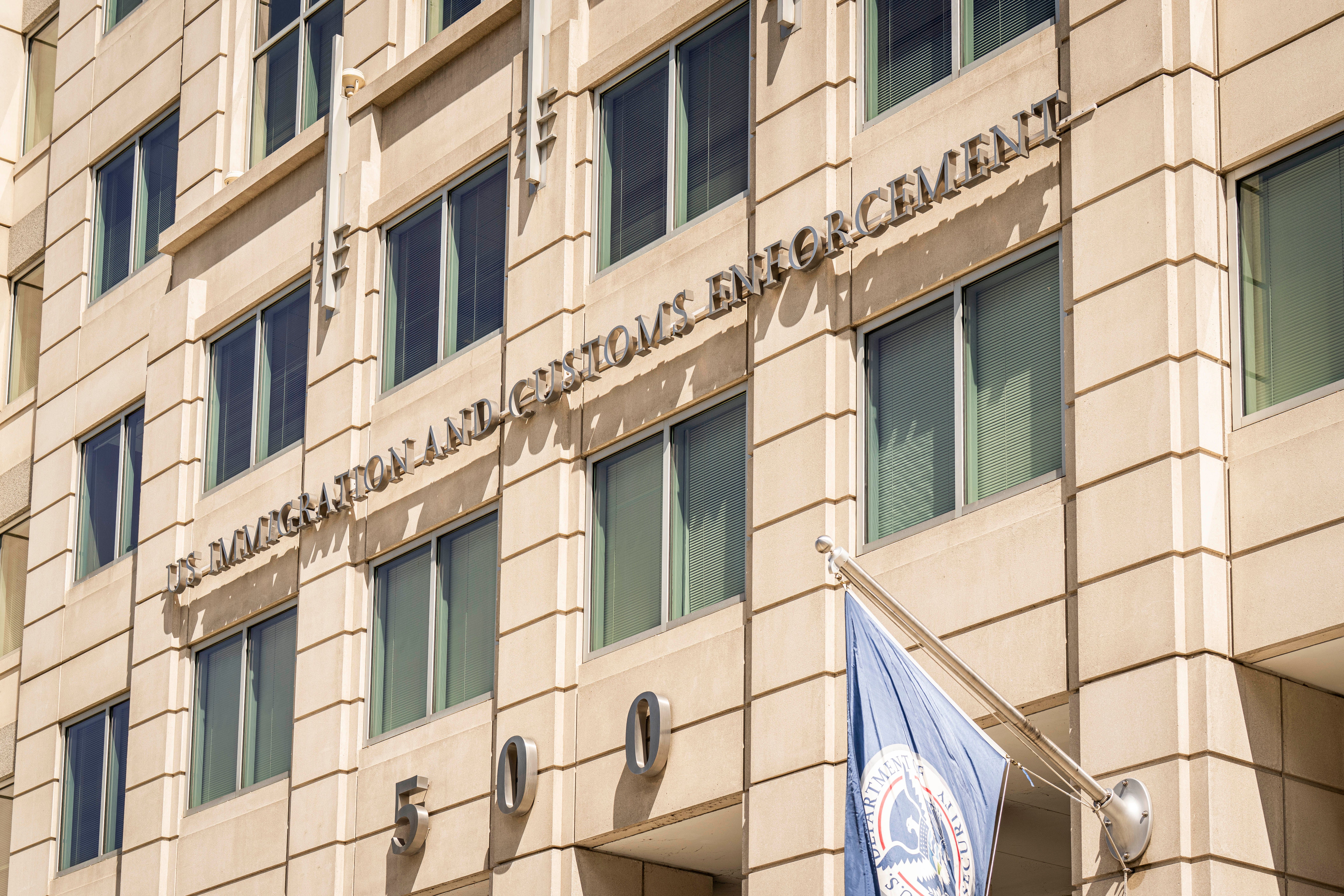 Facade of U.S. Immigration and Customs Enforcement building with agency letters and number 500, and a department flag flying in front.