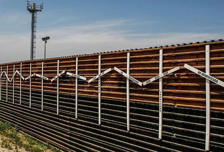 Mexico–United States barrier at the border between Tijuana and San Diego, with surveillance tower in the background.  The crosses represent migrants who died in the crossing attempt, some identified, some not. 