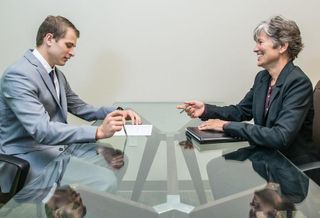An interviewer and interviewee during a job interview in a sparsely decorated conference room.