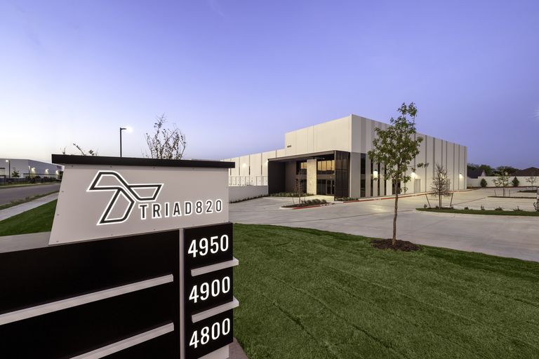 Modern industrial building with a sign reading "TRIAD820" and address numbers, set in a landscaped area during a clear day.