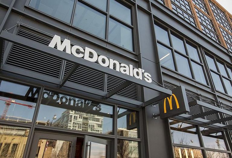 Exterior of a McDonald's restaurant with large glass windows and a white logo on a black facade, featuring the iconic yellow "M" sign.