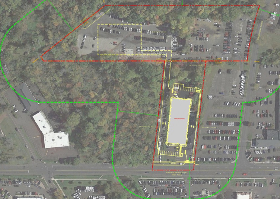 Aerial view of a parking area with rectangular lot outlined in yellow, surrounded by trees. Red and green lines indicate boundaries.