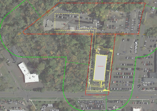 Aerial view of a parking area with rectangular lot outlined in yellow, surrounded by trees. Red and green lines indicate boundaries.