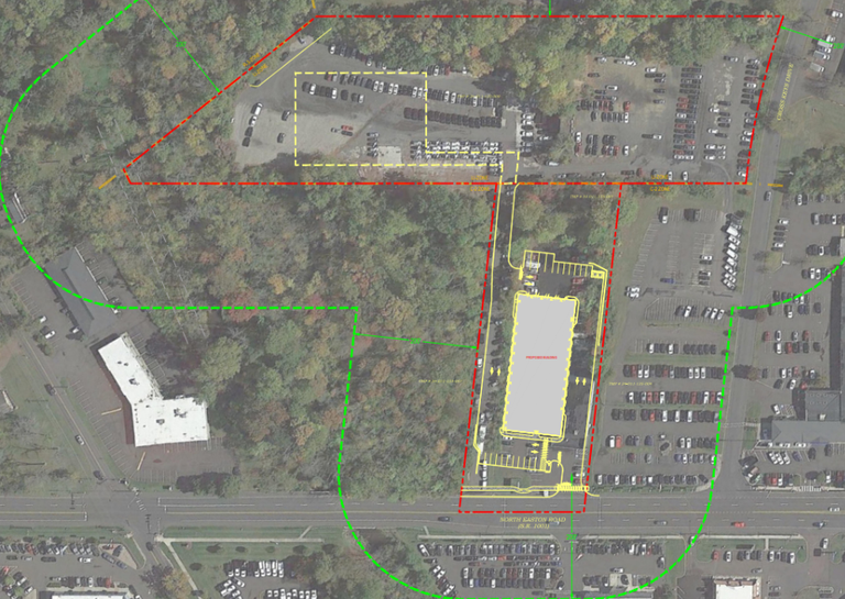 Aerial view of a parking area with rectangular lot outlined in yellow, surrounded by trees. Red and green lines indicate boundaries.