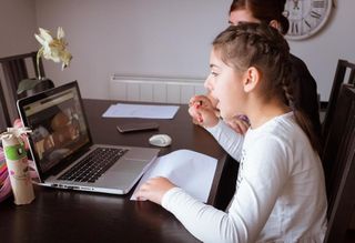 Two girls participating in remote schooling on a laptop at home.