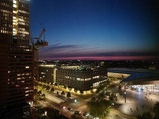 Cityscape at dusk with illuminated buildings, a construction crane, and a pink horizon beneath a deep blue sky.