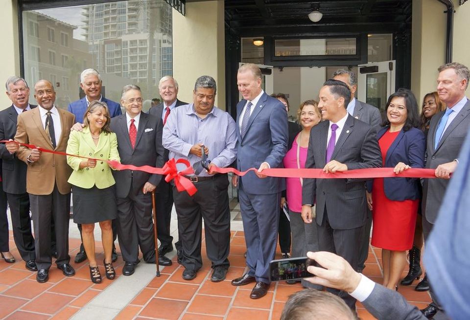 Resident Luis Milan cutting ribbon between San Diego Mayor Kevin Faulconer and San Diego Housing Commission CEO Richard Gentry at San Diego's Hotel Churchill