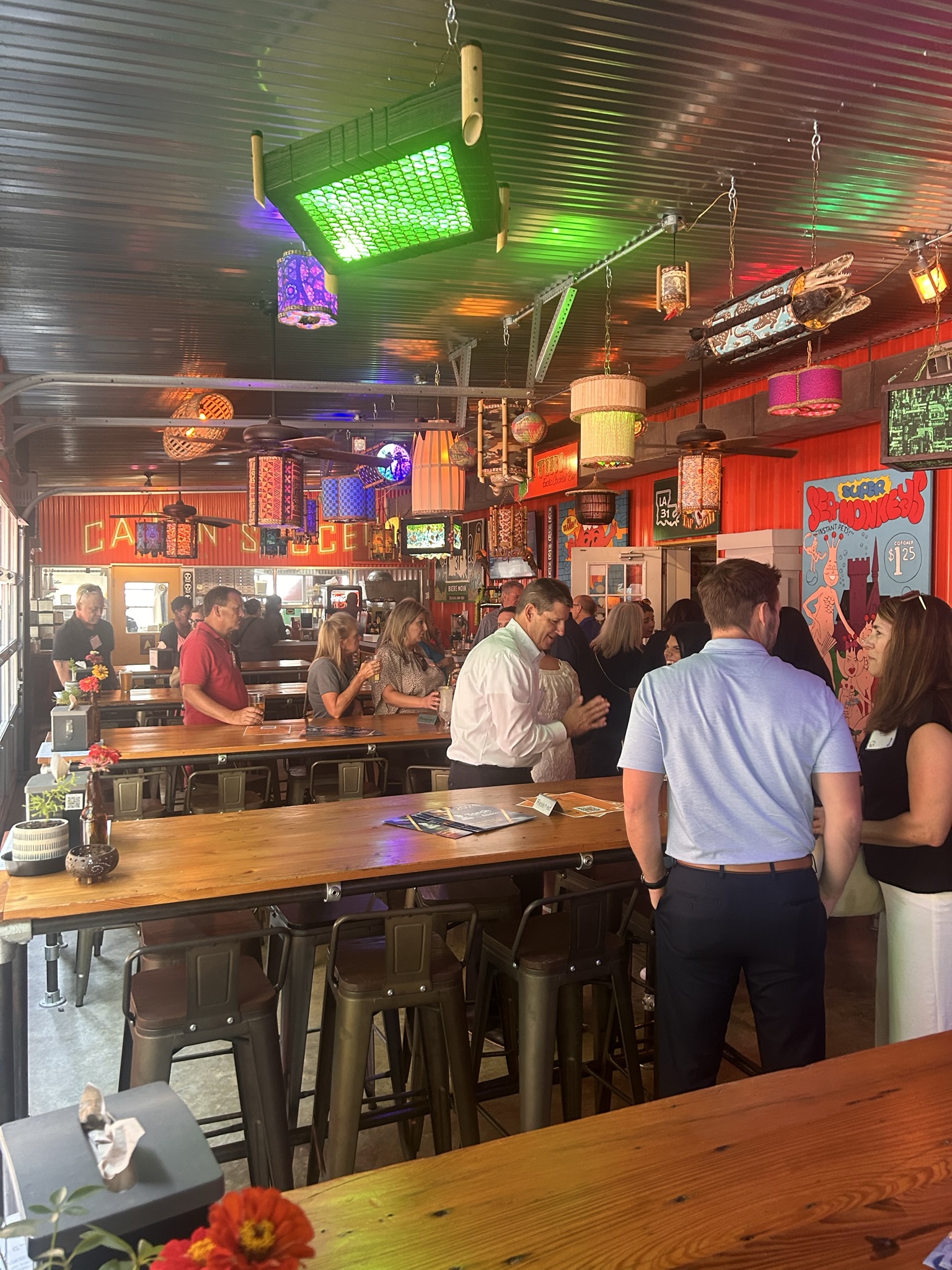 Group of people socializing in a colorful, vibrant bar with eclectic lighting and decor.