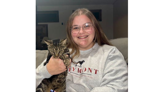 Greymont General Manager Annika, holding a tabby cat, sitting on a couch in a cozy room.
