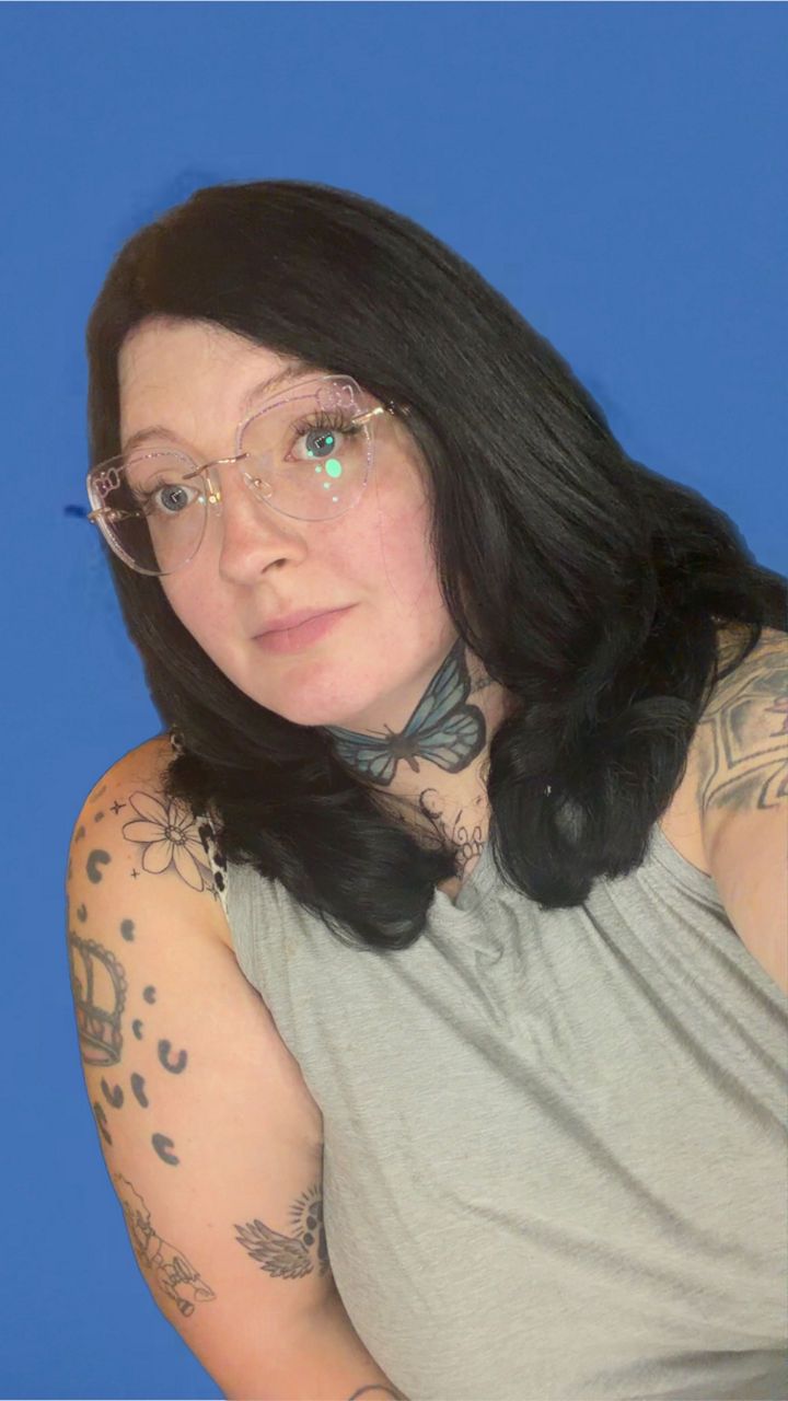 Michelle -Animal Care Attendant against a blue background. She has visible tattoos on her neck and arms.