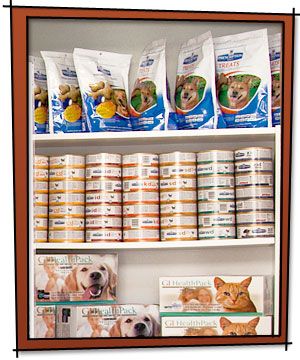 Shelves stocked with pet food, including bags of dog treats and cans of cat food, alongside boxed pet health packs featuring images of a dog and a cat.