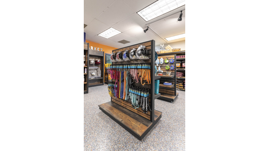 Pet store aisle with shelves displaying various leashes, collars, and retractable leads in assorted colors and styles.