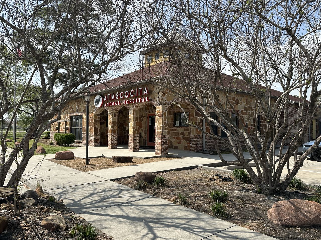 A stone building with a sign reading "Atascocita Animal Hospital" surrounded by trees and shrubs on a sunny day.