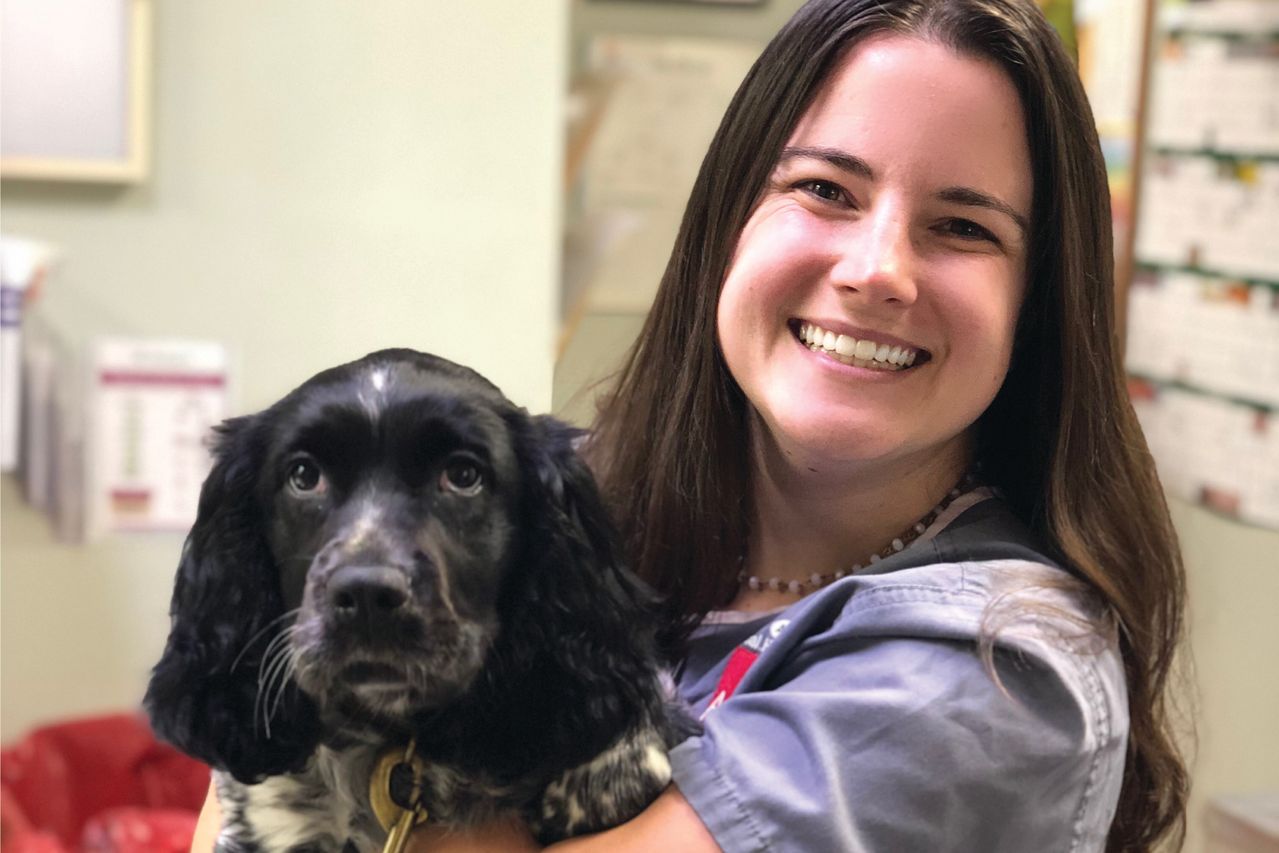 Smiling woman holding a black and white dog in an indoor setting.