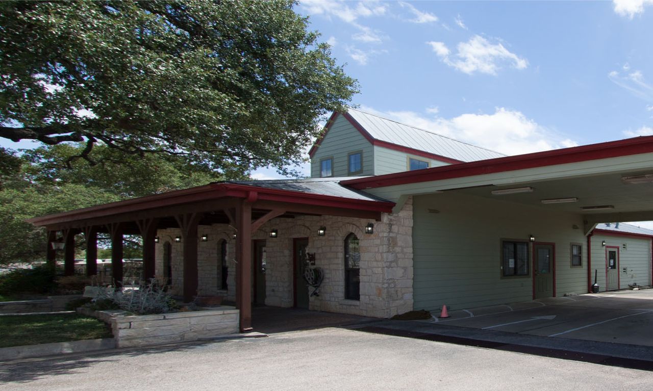 Hope Animal Clinic exterior. A stone and wood building with red accents and a covered entrance, set against a blue sky with scattered clouds and surrounded by trees.