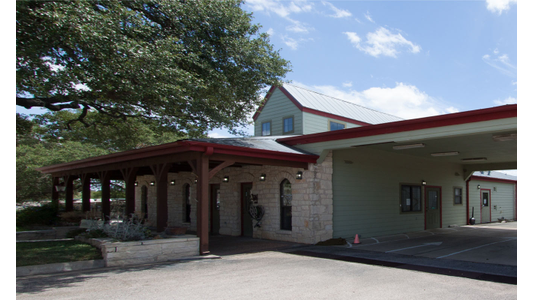 Hope Animal Clinic. A one-story building with a red roof and stone facade, partial shade from a large tree, and a porch with wooden columns on a sunny day.