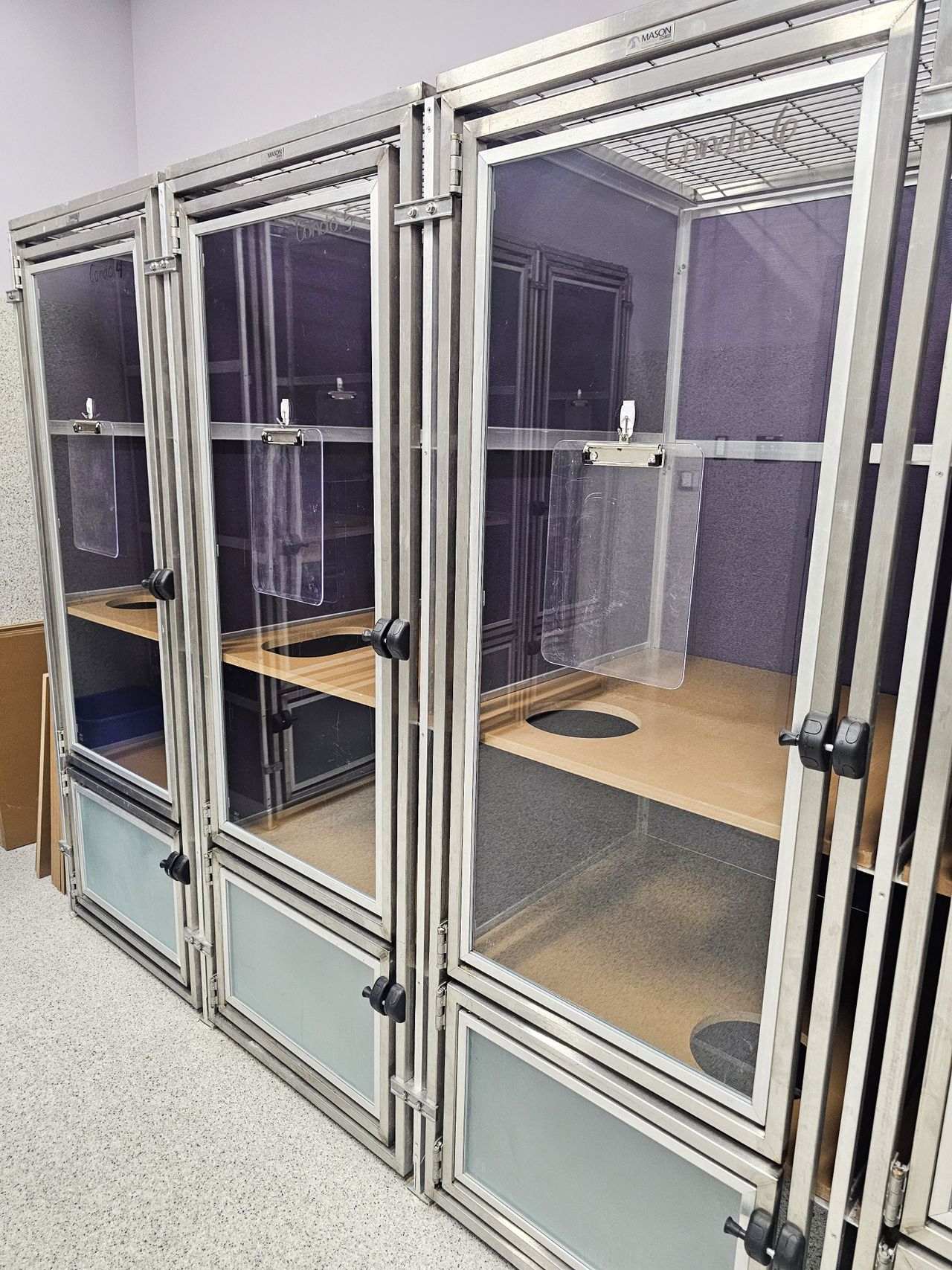 Three glass and metal cat condos with multiple compartments and lockable doors in a room with a speckled floor.