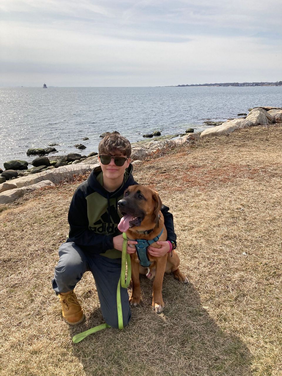 Maia -Animal Care Attendant with a brown dog on a leash sitting happily beside them.