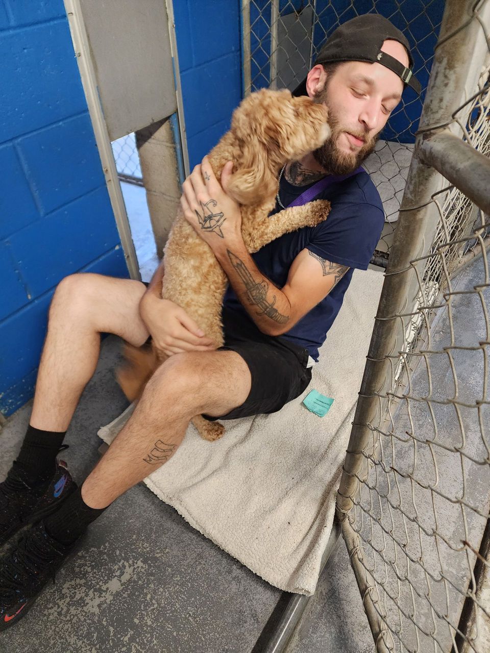 Daniel -Animal Care Attendant affectionately holding and being licked by a small curly-haired dog.