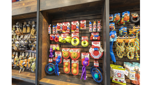 Shelves stocked with colorful dog toys, including balls, ropes, and chew toys, alongside popcorn bags in a pet store display.