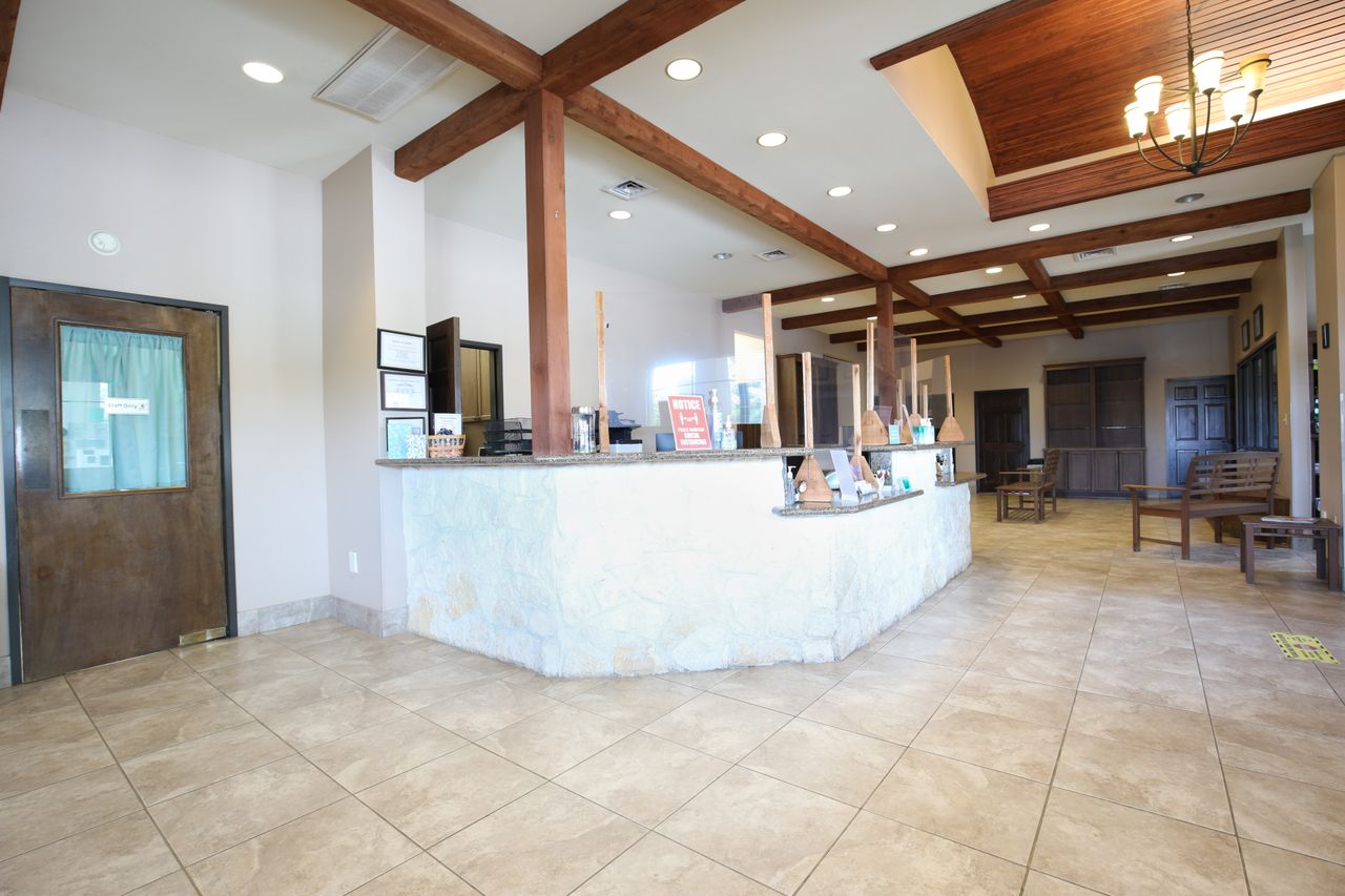 All Community Animal Hospital's spacious lobby area with a tiled floor, a reception desk with protective barriers, and seating along the walls under a wooden ceiling.