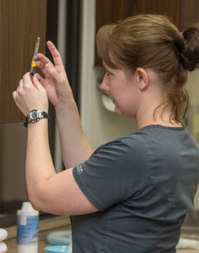 A woman in scårubs carefully preparing a syringe, focusing intently.