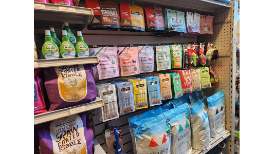 K9 Kaos store shelf displaying various cat treats, bags of dry cat food, and bottles of pet breath freshener.