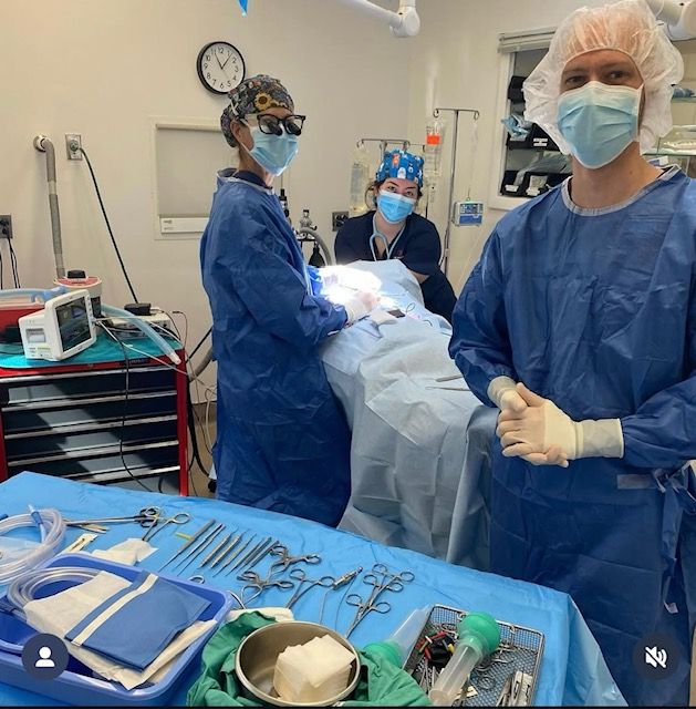 Medical team performing surgery in an operating room, wearing blue scrubs and masks. Surgical tools are neatly arranged in the foreground.